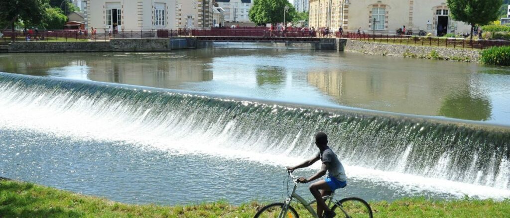 Un cycliste longe une chute d’eau devant la Maison de l’Eau au Mans, un lieu emblématique du parc de l’Arche de la Nature, idéale balade à vélo au Mans.