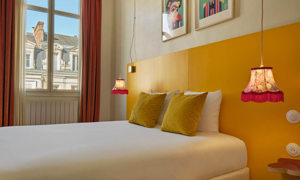 Chambre Lounge hôtel Artyster Le Mans, lit double cosy, décoration vintage chic, vue sur les toits du centre-ville.