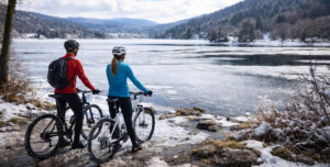 Couple à vélo au bord du lac d’Aydat en hiver près de Clermont-Ferrand avec paysage volcanique enneigé